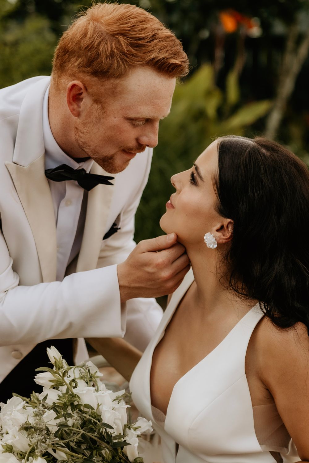 Intimate wedding portrait featuring classic white tuxedo and elegant white gown with bouquet.