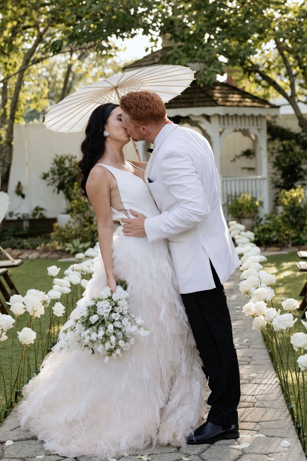 Intimate wedding moment captured under parasol with white floral garden path.