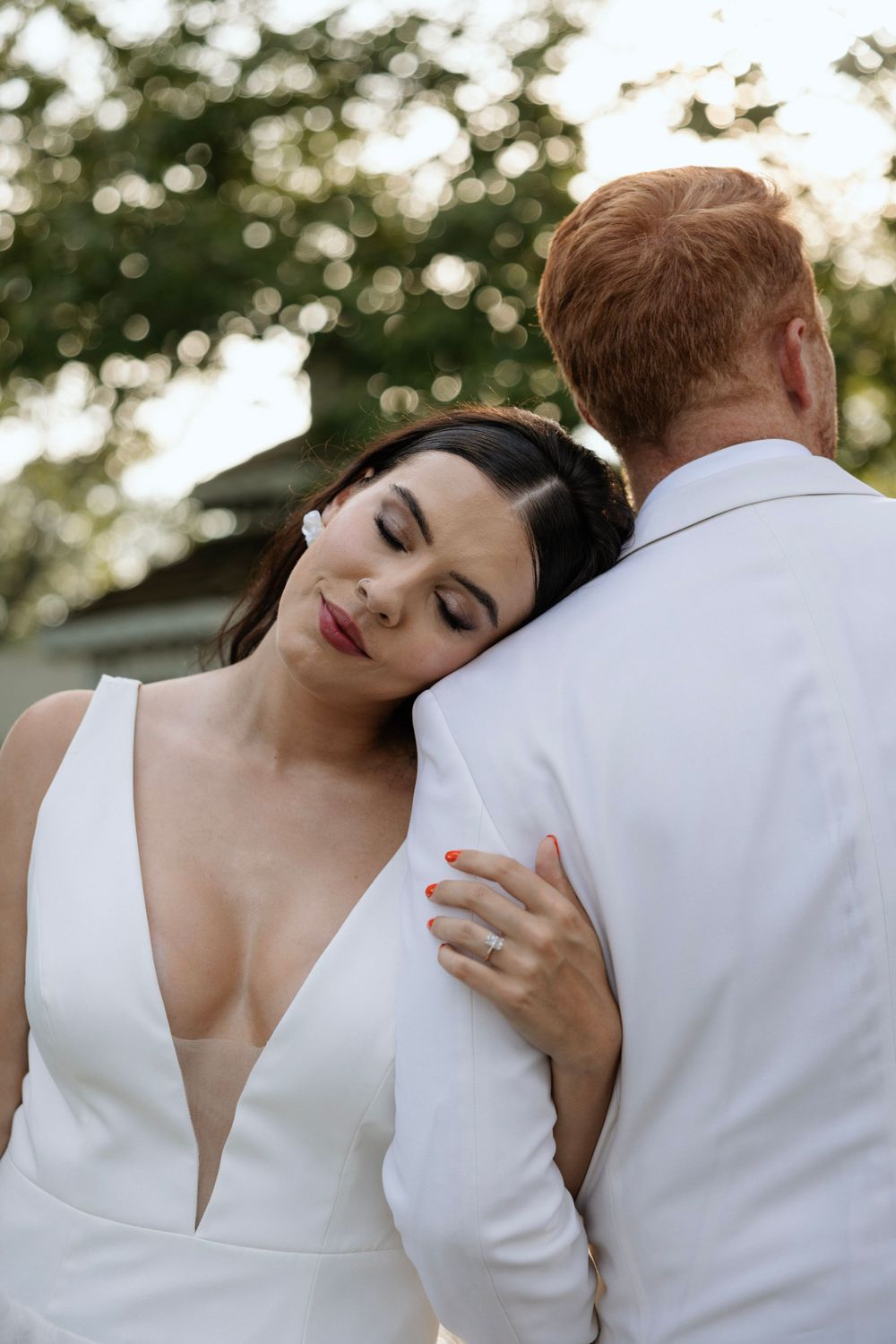 Intimate embrace between newlyweds in white attire during outdoor garden photoshoot.