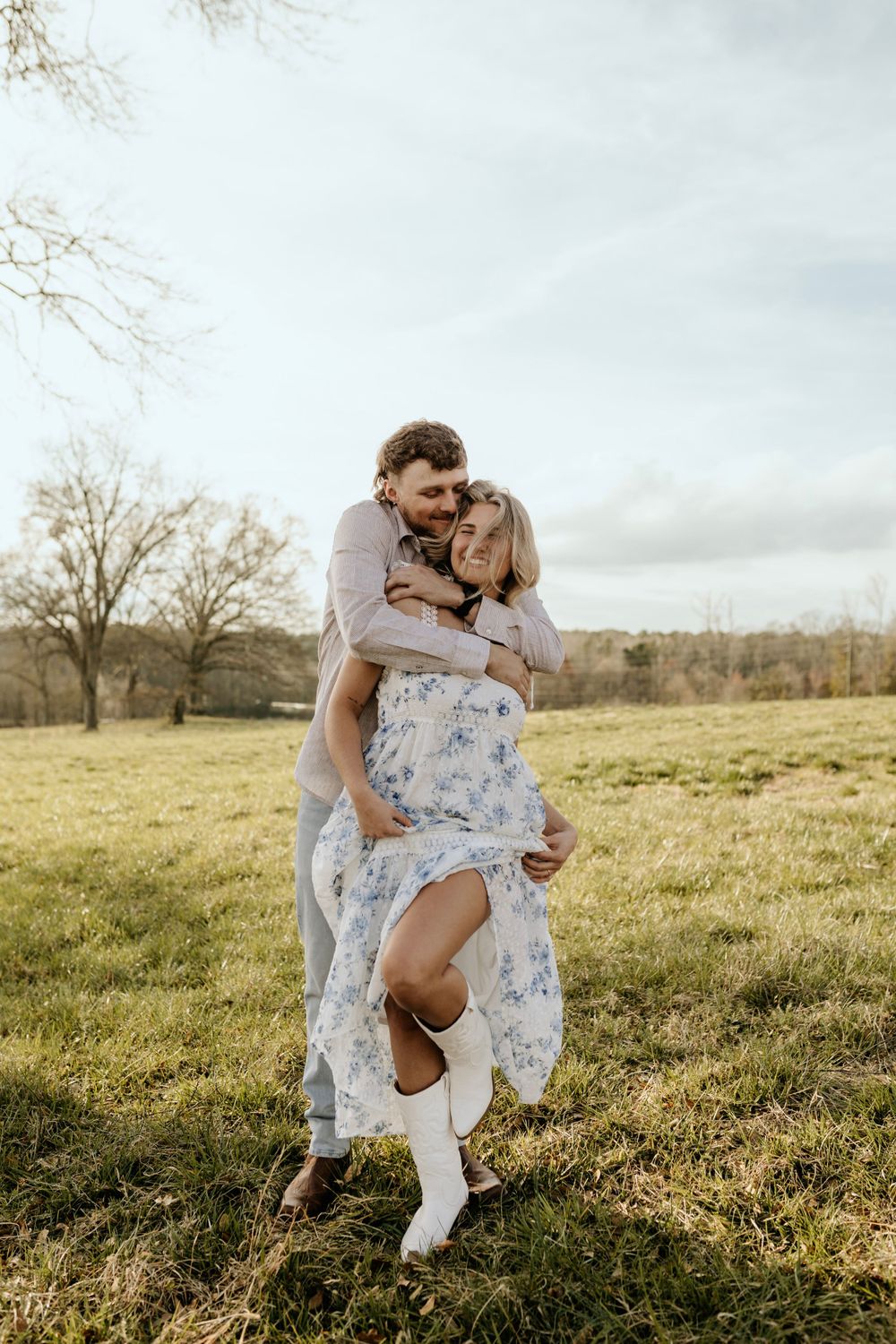 A playful moment captured between a couple in a sunny field wearing casual wedding attire.