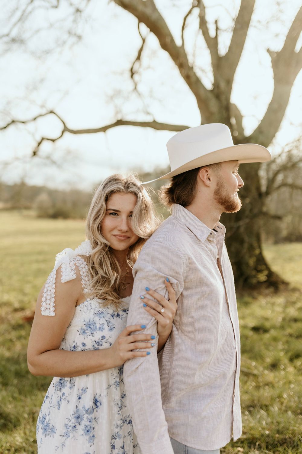 A sunlit portrait of a couple in country attire sharing an intimate moment by a tree.