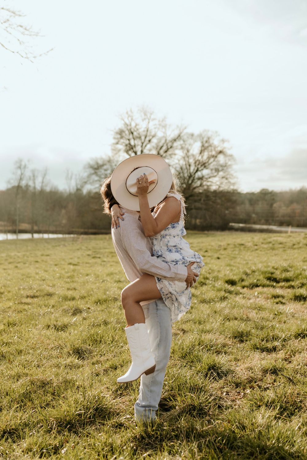 A joyful embrace in a sun-drenched field with western attire and romantic styling.