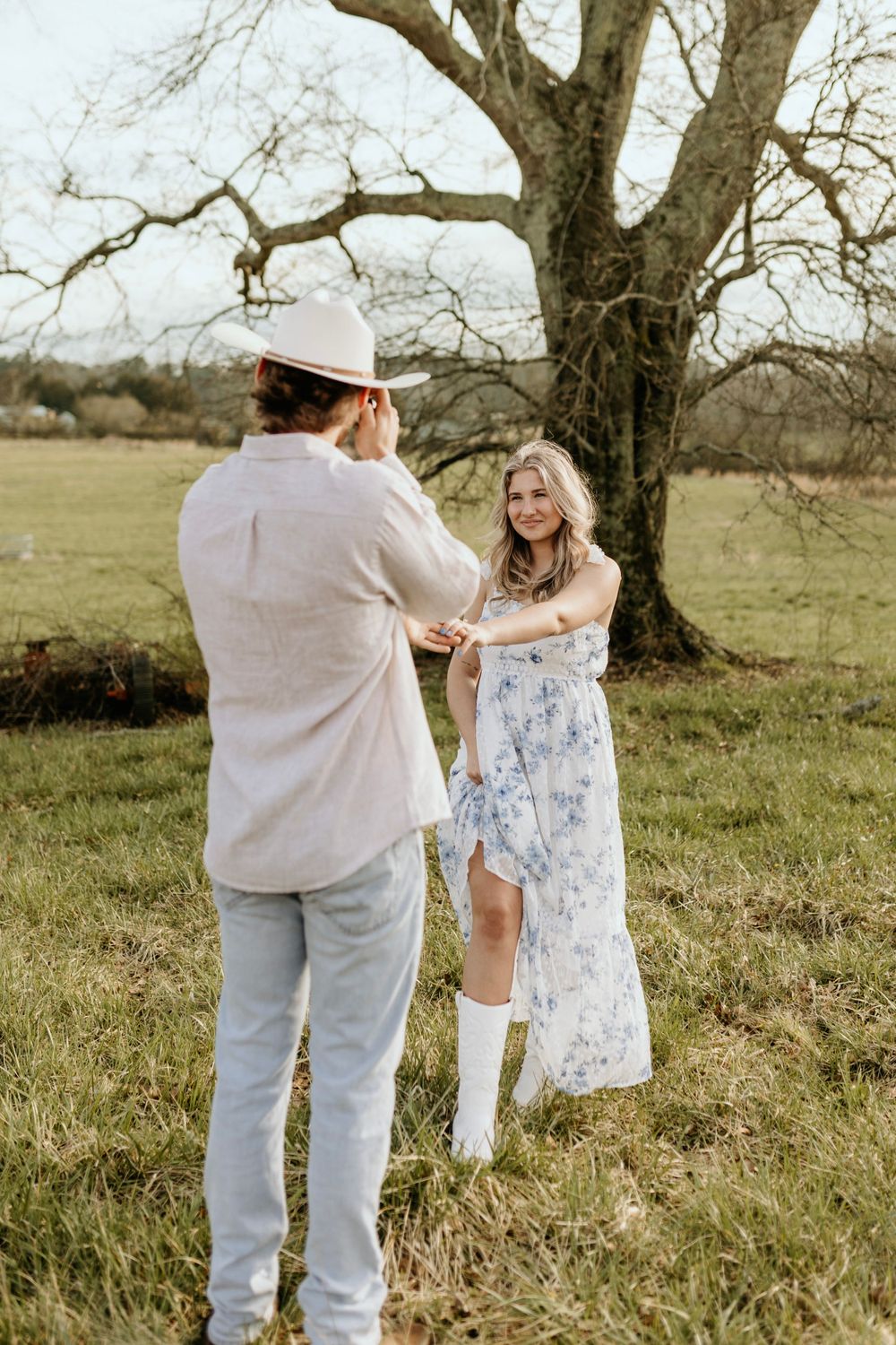 A couple in country attire dancing playfully in a rustic field setting.