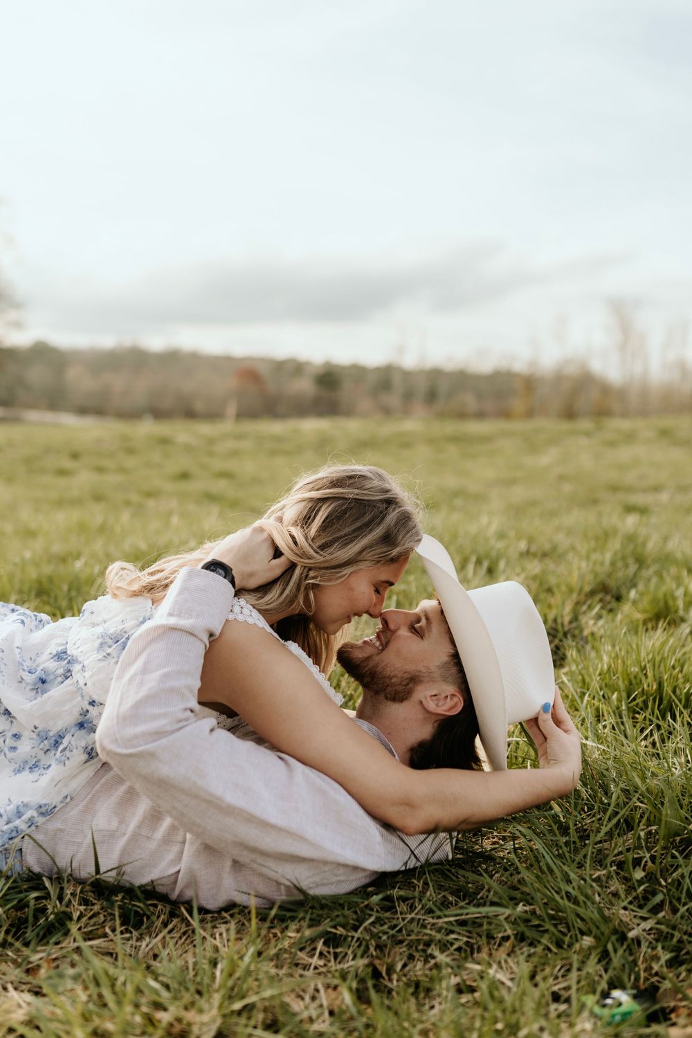 A tender moment between a couple lying in grass with countryside scenery behind them.
