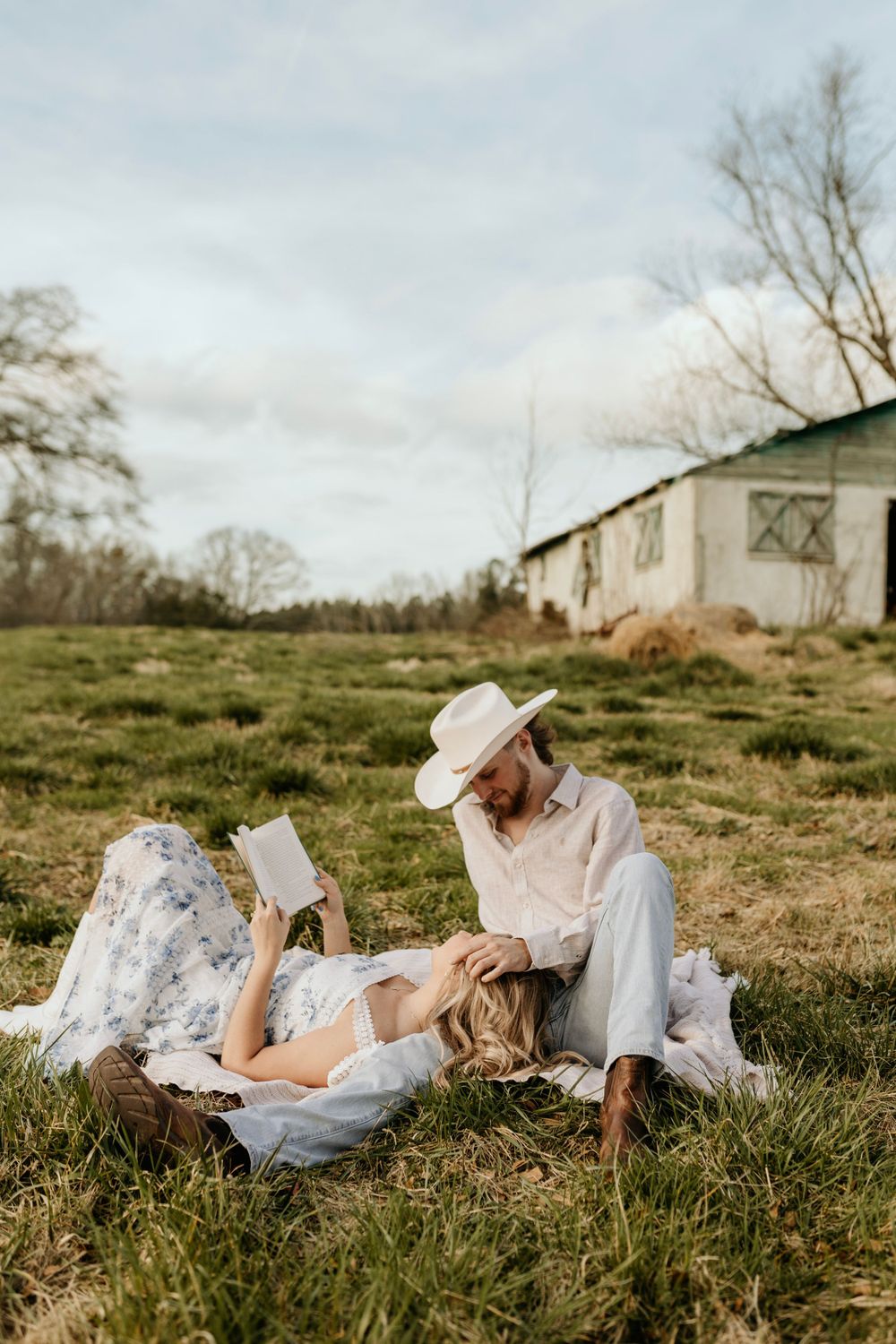 A couple shares a peaceful moment reading outdoors near a rustic barn.