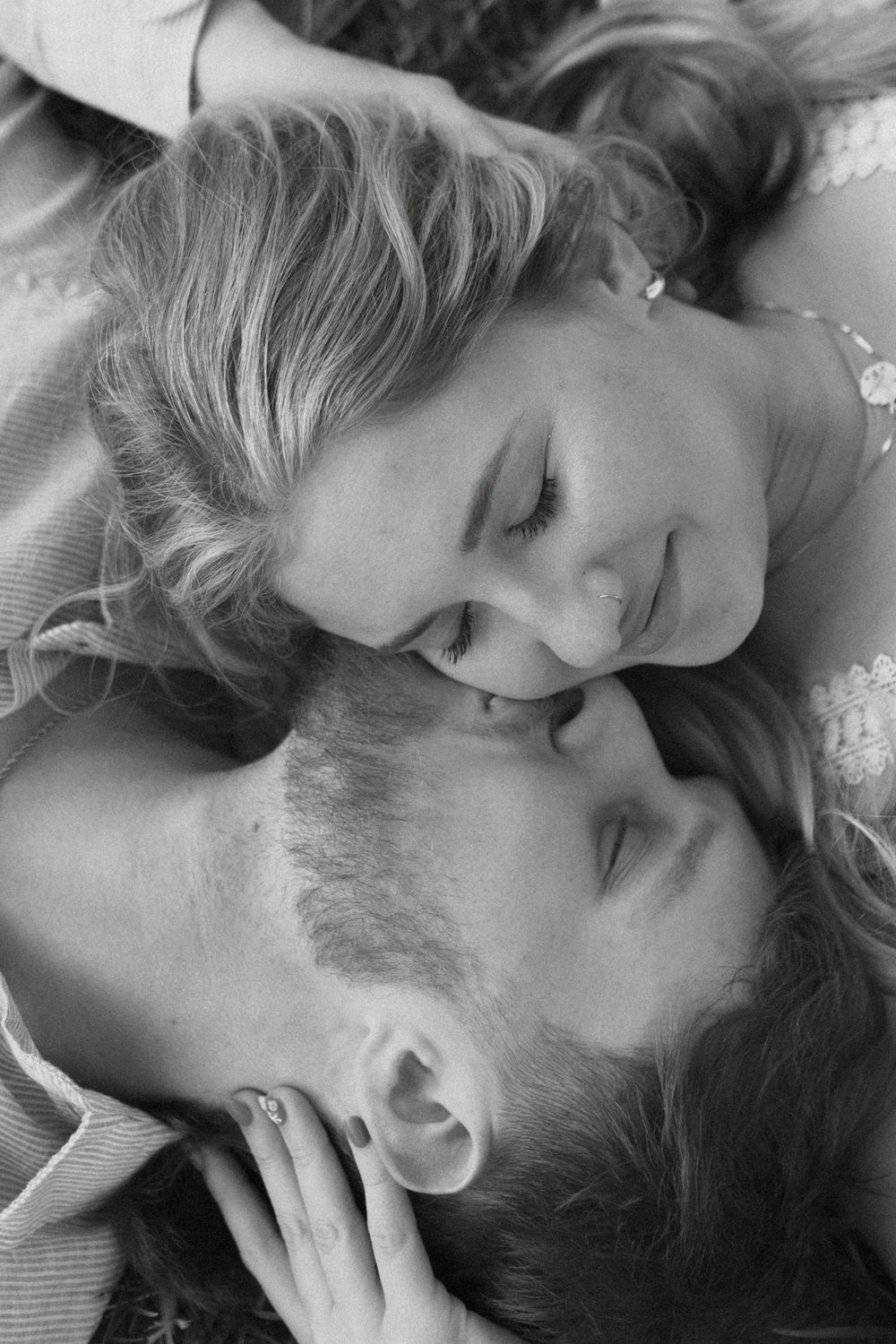An intimate black and white portrait of a couple lying close together.
