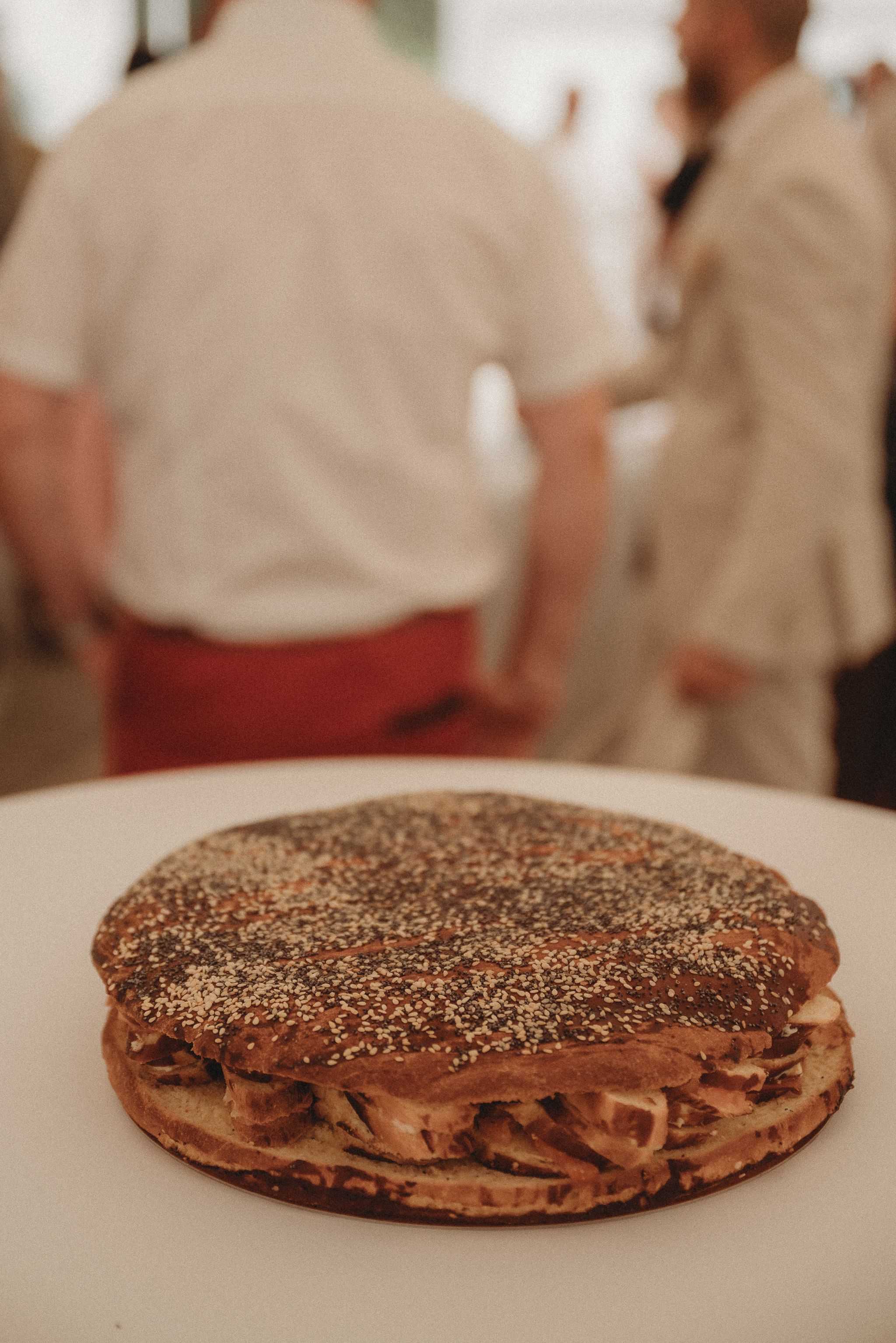 A large chocolate sandwich cookie with a creamy filling topped with poppy seeds on a white plate.