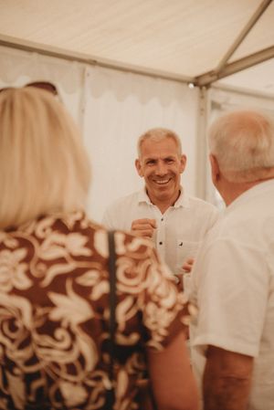 Guests engaged in conversation during a social gathering under a white tent.