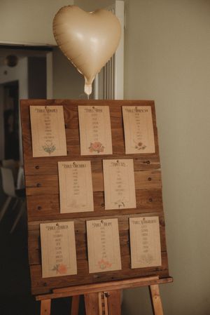 A wooden seating chart display with paper cards and a gold heart balloon on top.