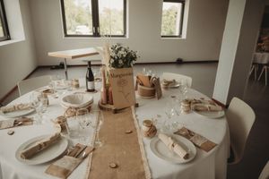 Wedding reception tables decorated with burlap runners, white plates and natural centerpieces in a bright venue.