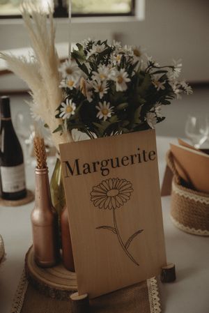 Rustic brown paper floral centerpiece with daisies and dried flowers labeled 'Marguerite' on a decorated table.