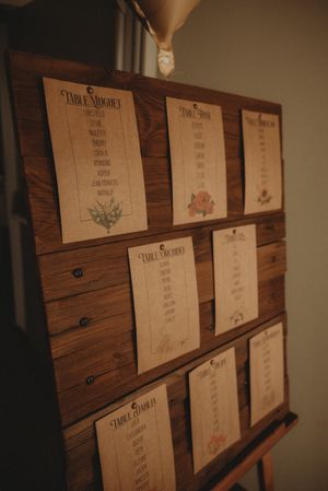 Wooden seating chart display with multiple paper cards showing table assignments for an event.