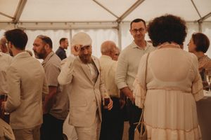 Wedding reception gathering under a white tent with guests mingling in light colored attire.