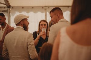 Social gathering of guests in light colored attire under a white tent canopy.