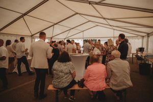 Reception event under a white tent with guests seated and standing around tables.