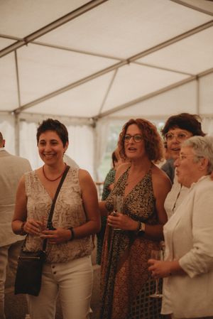 Wedding guests in summer attire enjoying drinks and conversation under a white tent.