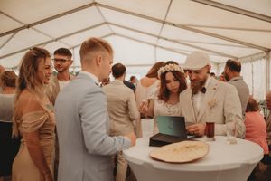 Wedding celebration under white tent with guests gathered around cocktail tables.