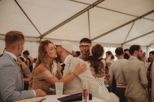 Wedding guests celebrating and embracing during lively reception under white tent.