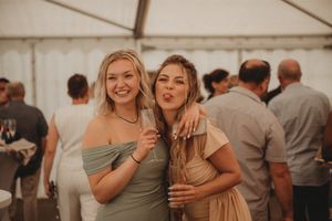 Two guests pose together during celebration under white tent with warm lighting.