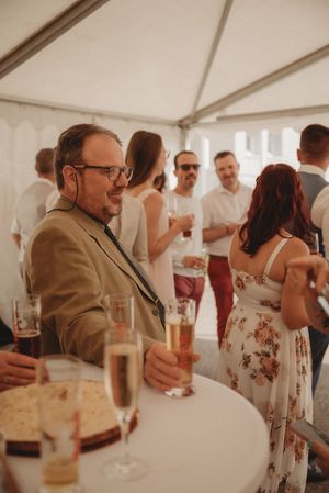 Guests mingling at reception with champagne and refreshments under white tent.