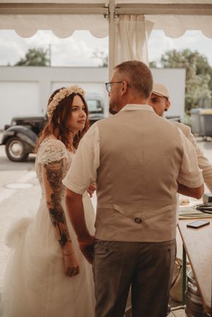 Guest in floral crown and wedding dress with colorful arm tattoos at outdoor reception.
