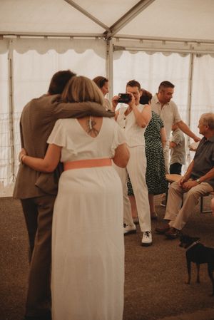 Wedding guests dancing and socializing under a white tent at a reception.