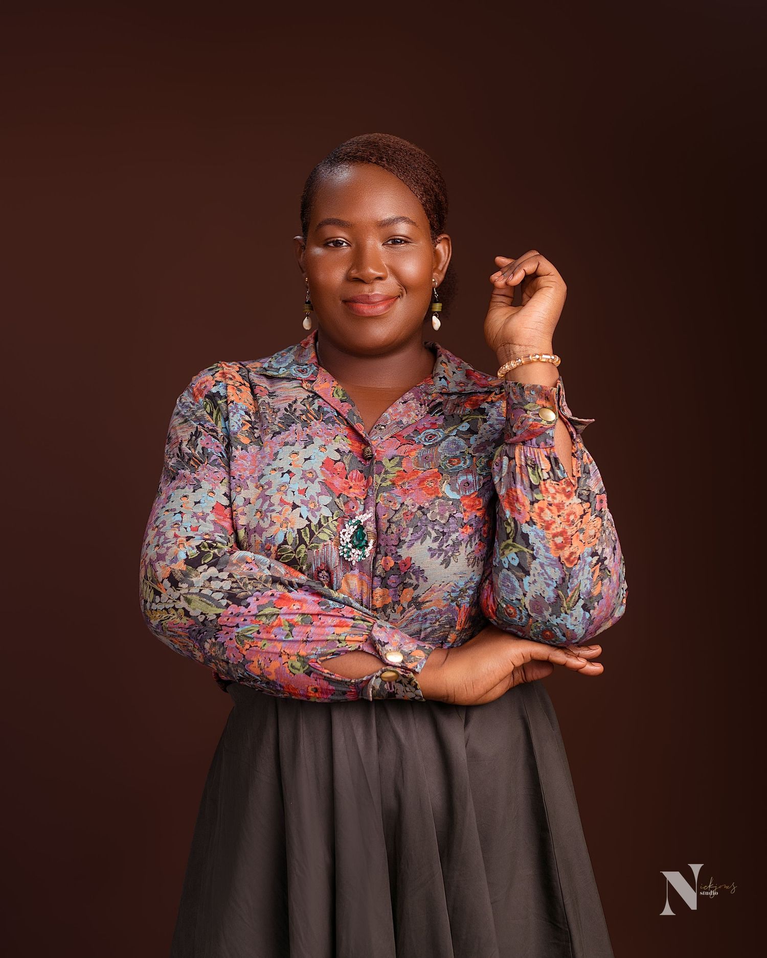 A portrait of someone in a floral print blouse and dark skirt against a brown background.