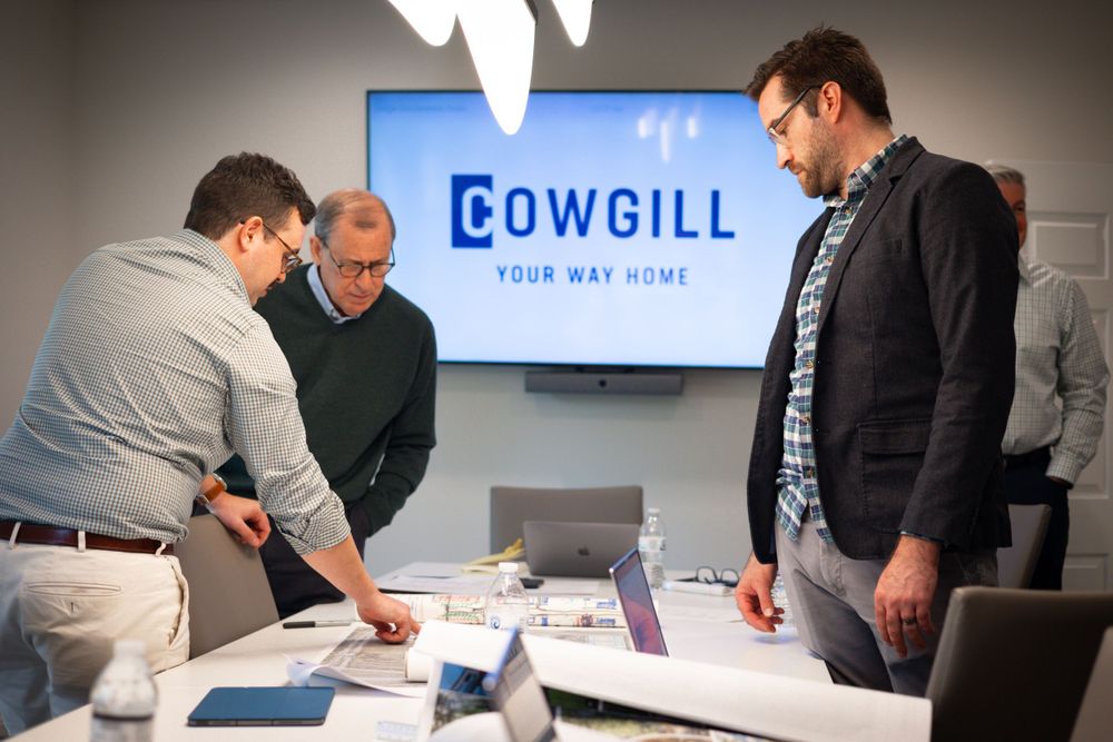 Business team reviewing documents in conference room with Cowgill logo displayed.