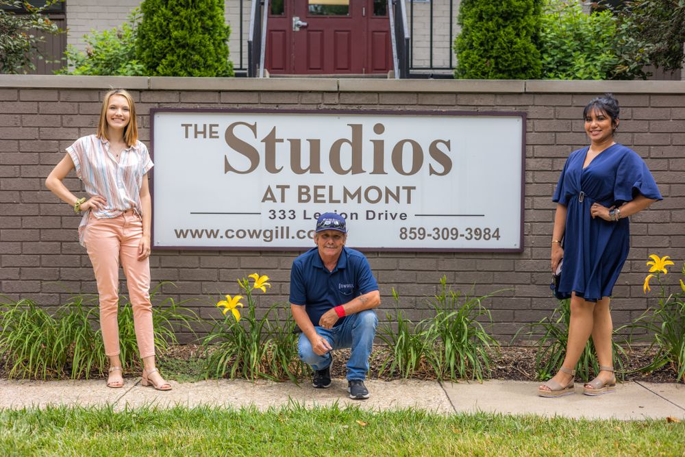People posing casually along brick wall with 'The Studios' signage outdoors.
