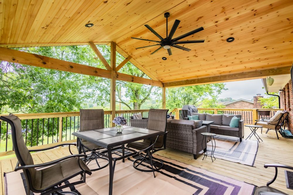Covered deck with wood ceiling, ceiling fan, and outdoor furniture overlooking natural scenery.