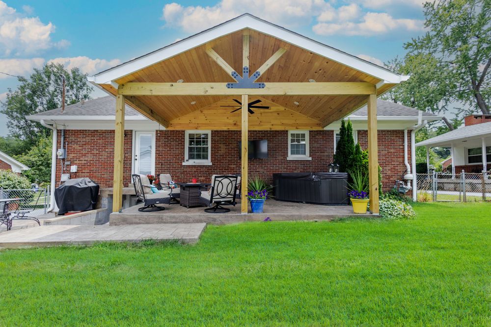Modern covered patio with exposed wooden beams and comfortable seating area attached to brick home.