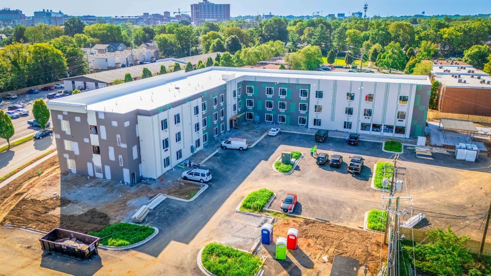 Aerial view of modern apartment complex with white facade and parking lot surrounded by trees.