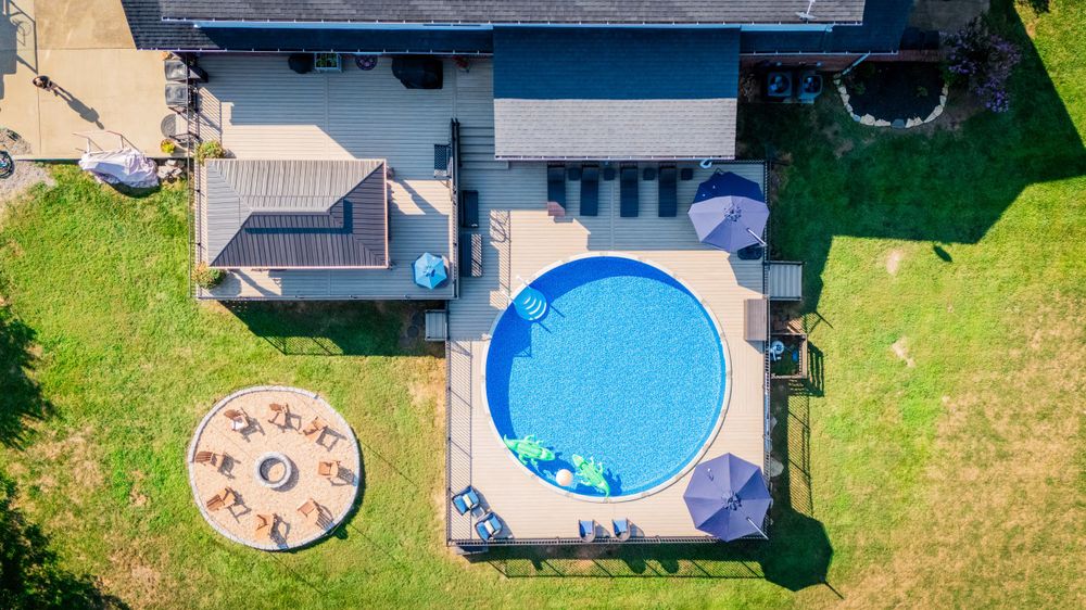 Aerial view of backyard with round pool, concrete deck, and landscaped patio spaces.