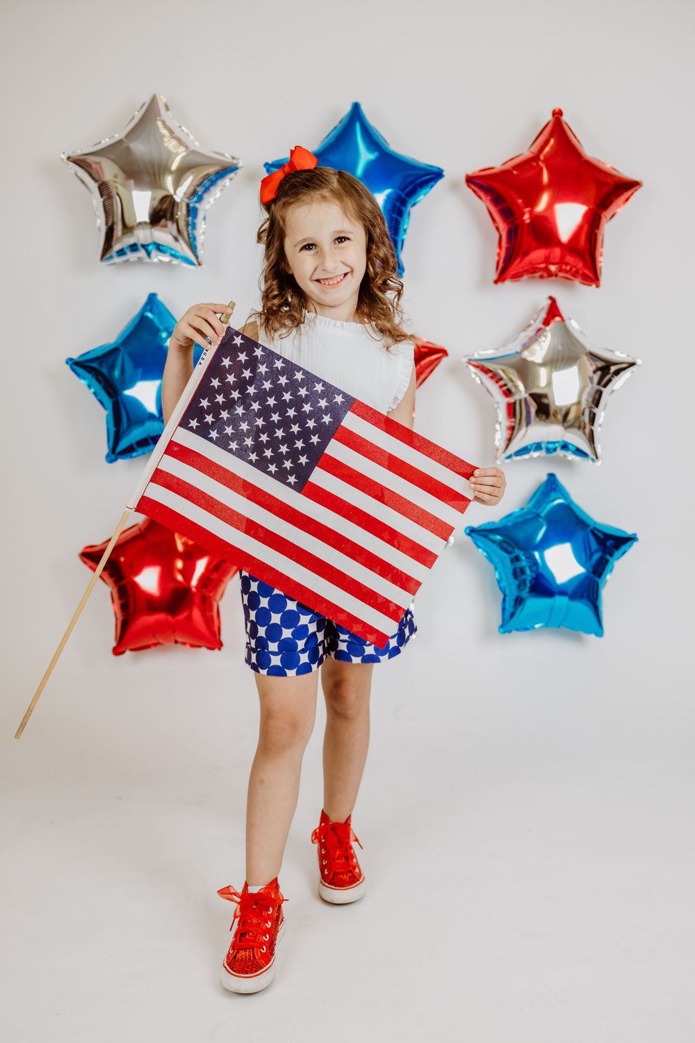 Patriotic pose with American flag surrounded by red, white and blue star balloons.