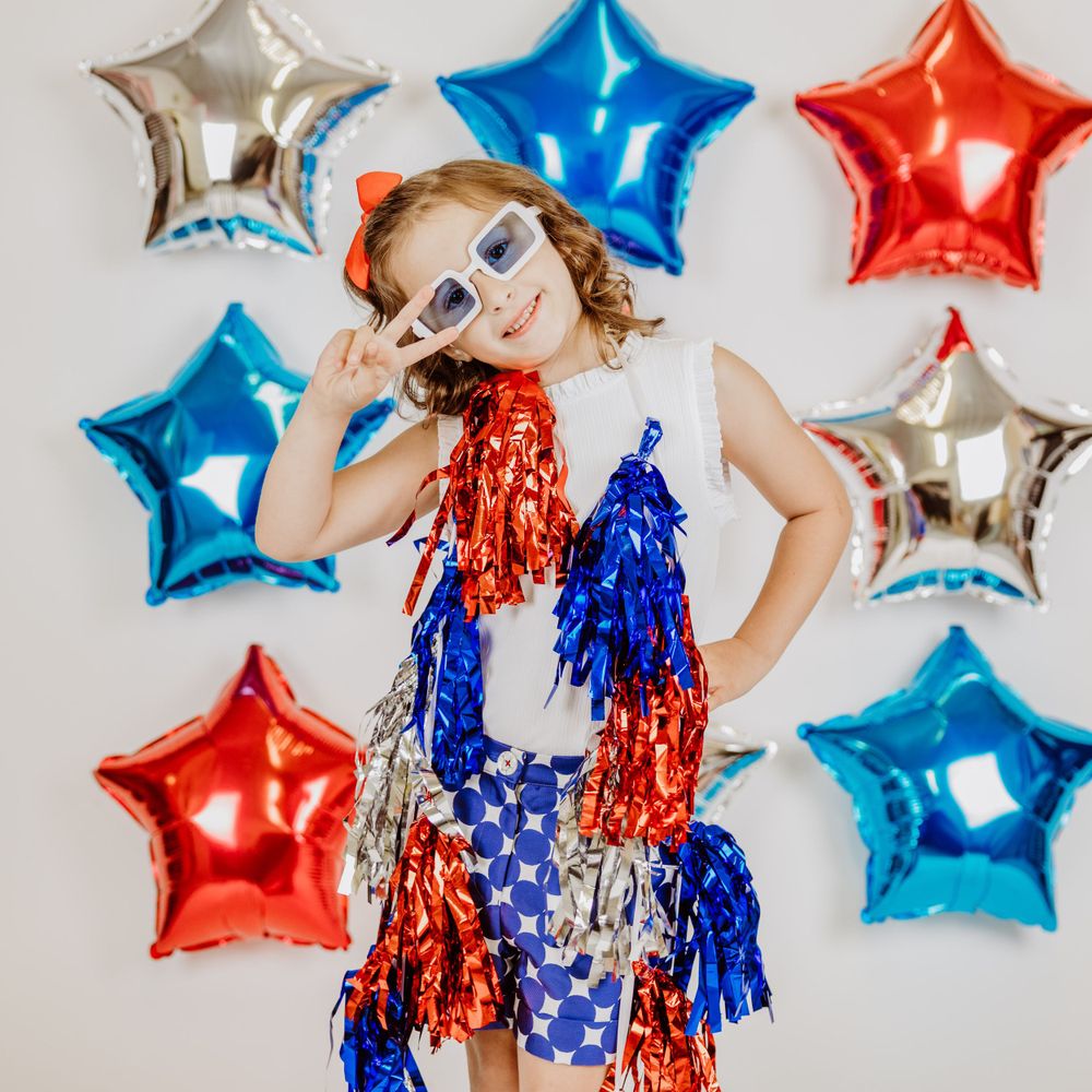 Patriotic photo setup with red, white and blue star balloons and tinsel decorations against a white background.