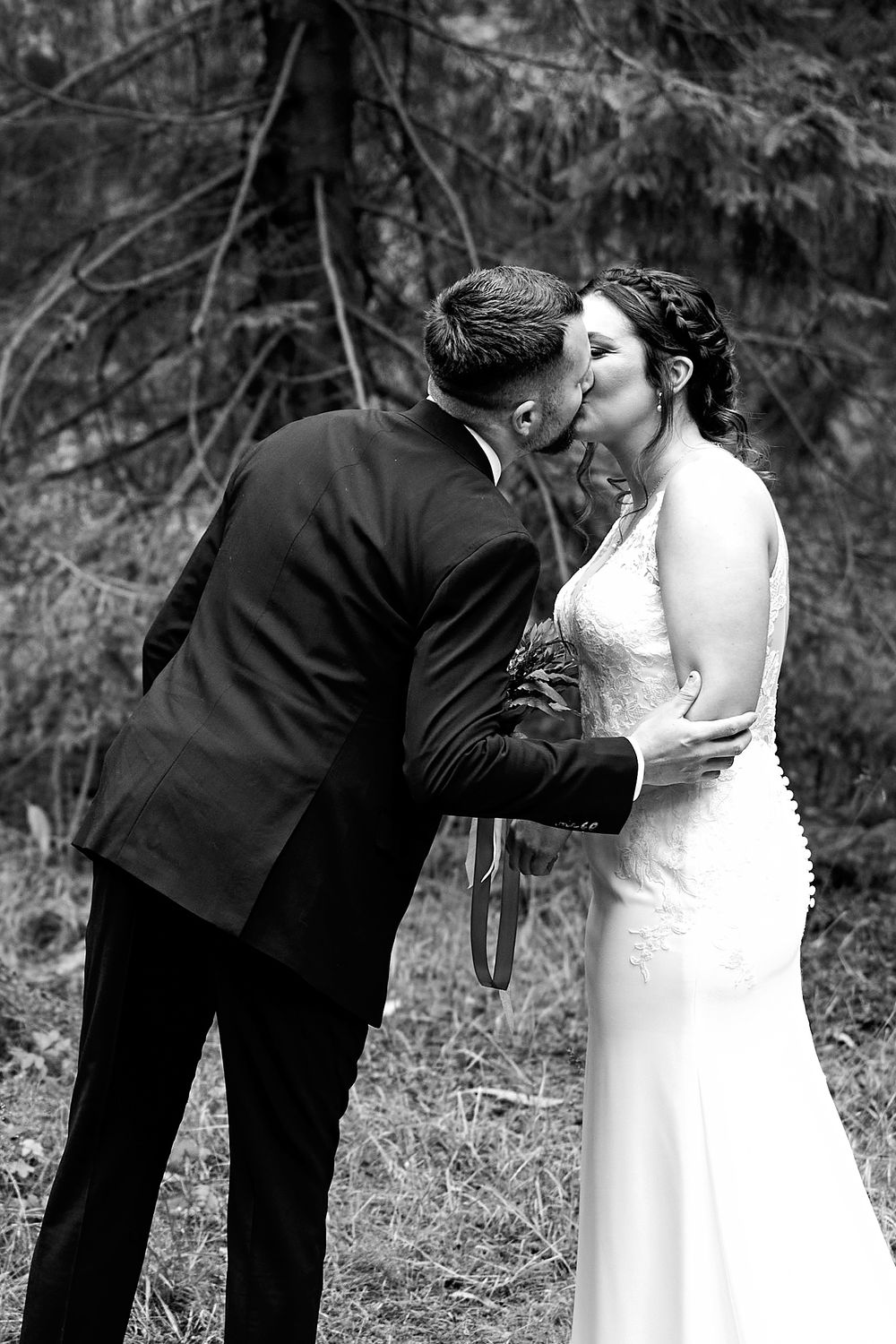 Black and white intimate wedding portrait captured in a peaceful forest setting.