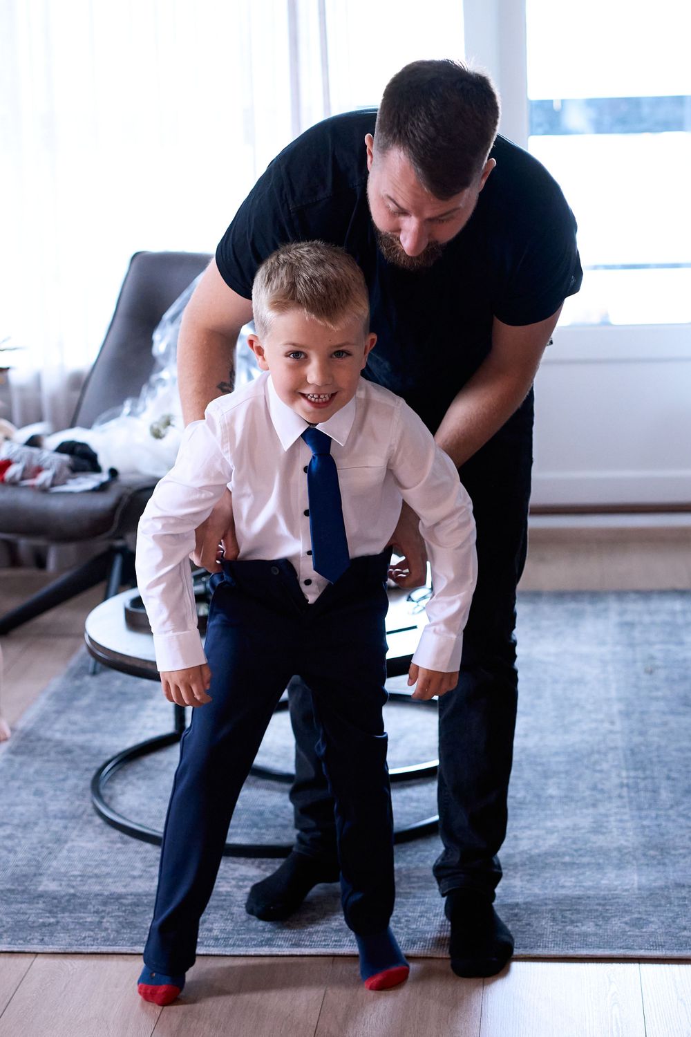 Playful moment during formal dressing with matching navy suits and tie.