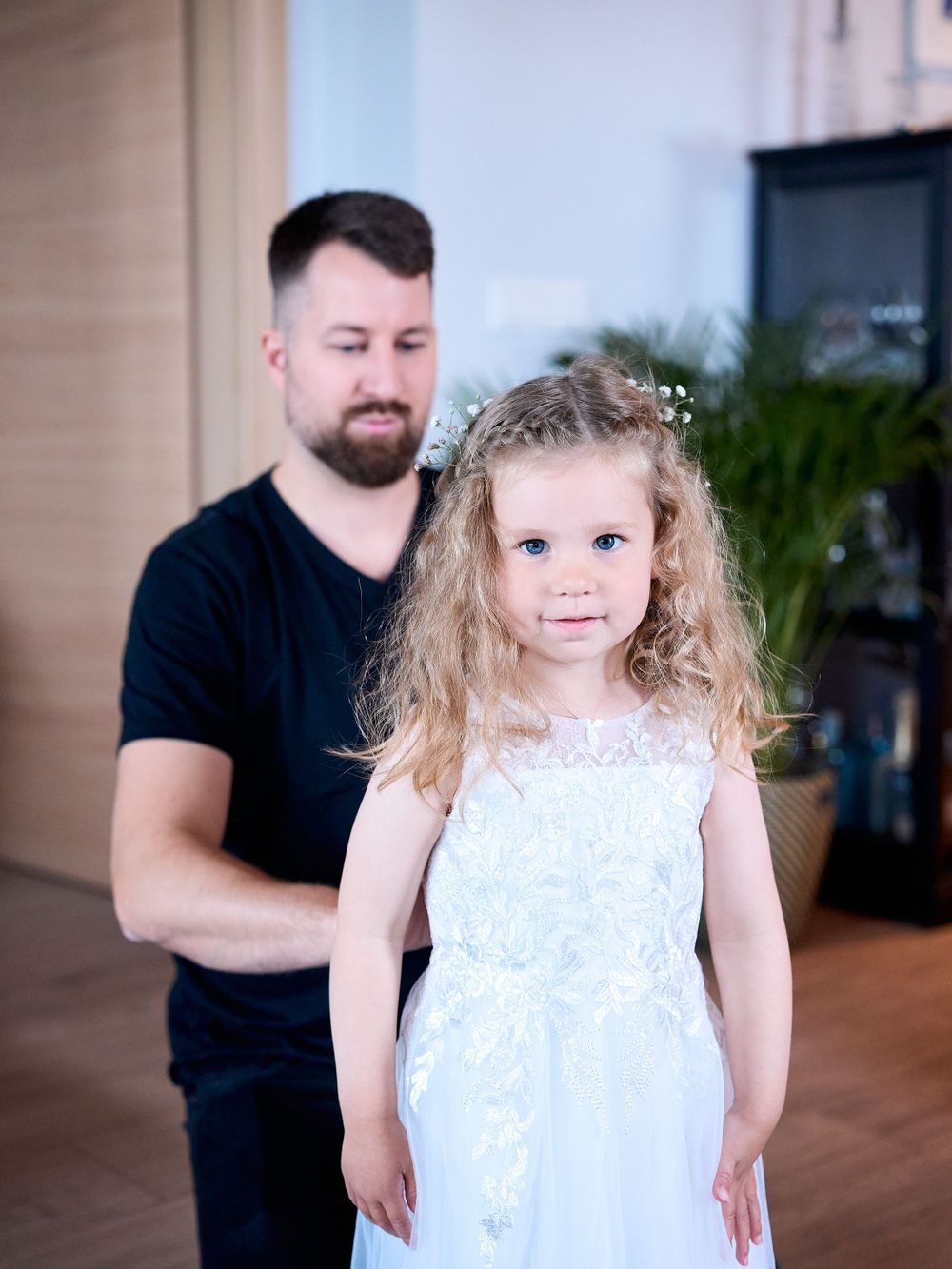 Little girl in white lace dress stands in front of wedding venue.