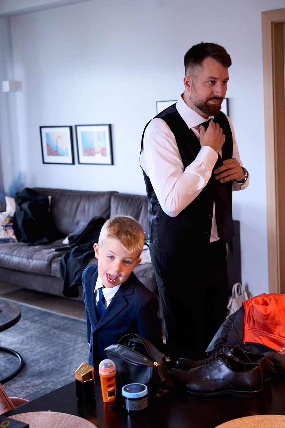 Formal preparation scene with navy suits and dress shoes visible in living room setting.