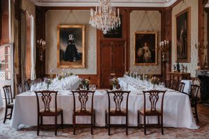 Elegant dining room with crystal chandelier, white tablecloths, and antique wooden chairs surrounded by portrait paintings.