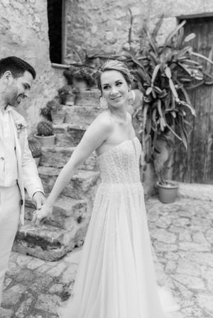 A black and white photo of a couple sharing a joyful moment against a rustic stone wall.