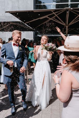 Wedding guests shower the newlyweds with confetti under a patio umbrella during the celebration.