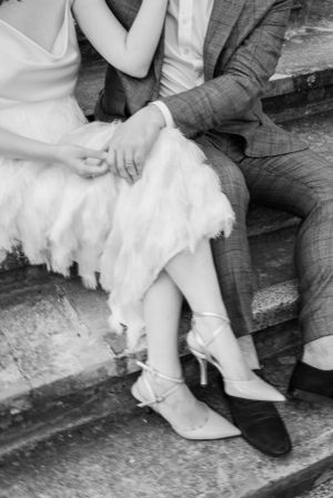 Black and white detail shot of wedding shoes and dress hem on stone steps.