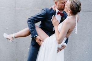Playful wedding portrait showing romantic dip pose against grey wall.