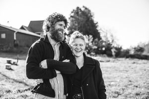 BW image of Husband and wife smiling in front of their home.