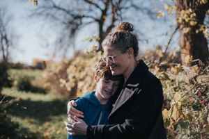 A mother hugs her adolescent son in her arms as they stand outside in the Fall.