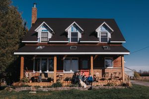 Beautiful little farm house with 3 windows and a family sitting outside.
