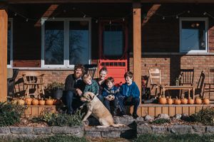 A family sits on their front porch surrounded by fall pumpkins and gourds.