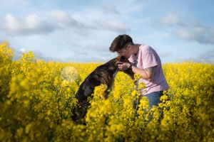 Jeune femme qui fait un bisous sur la tête d'un chien croisé dans un champs de colza
