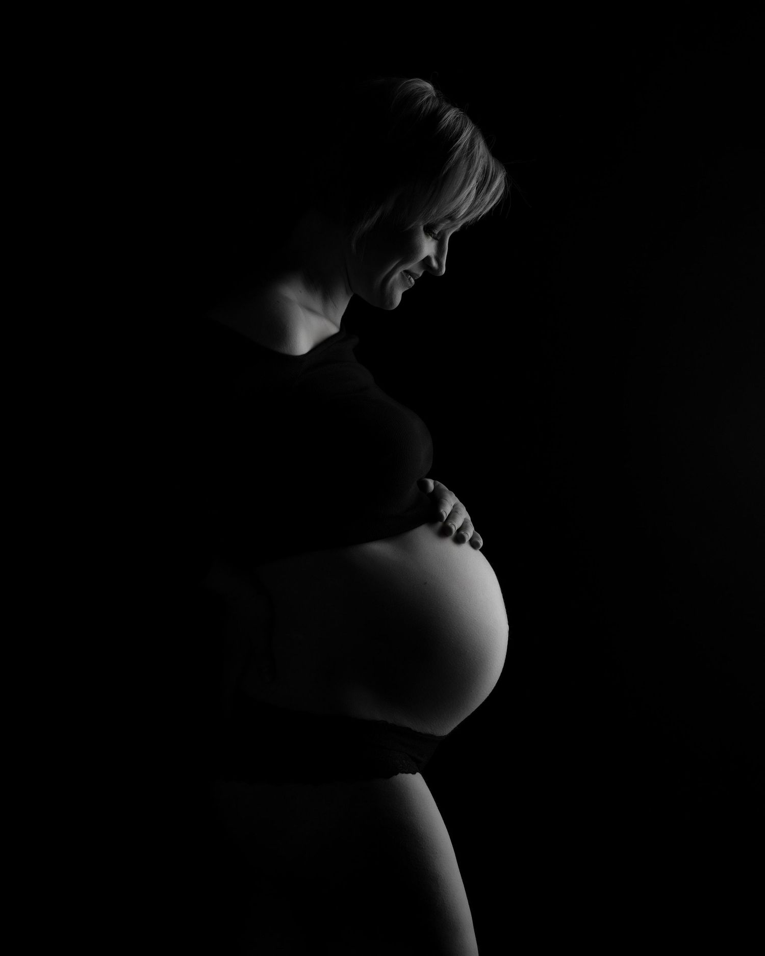 maternity photo shoot in studio, a pregnant woman looks warmly down at her baby bump